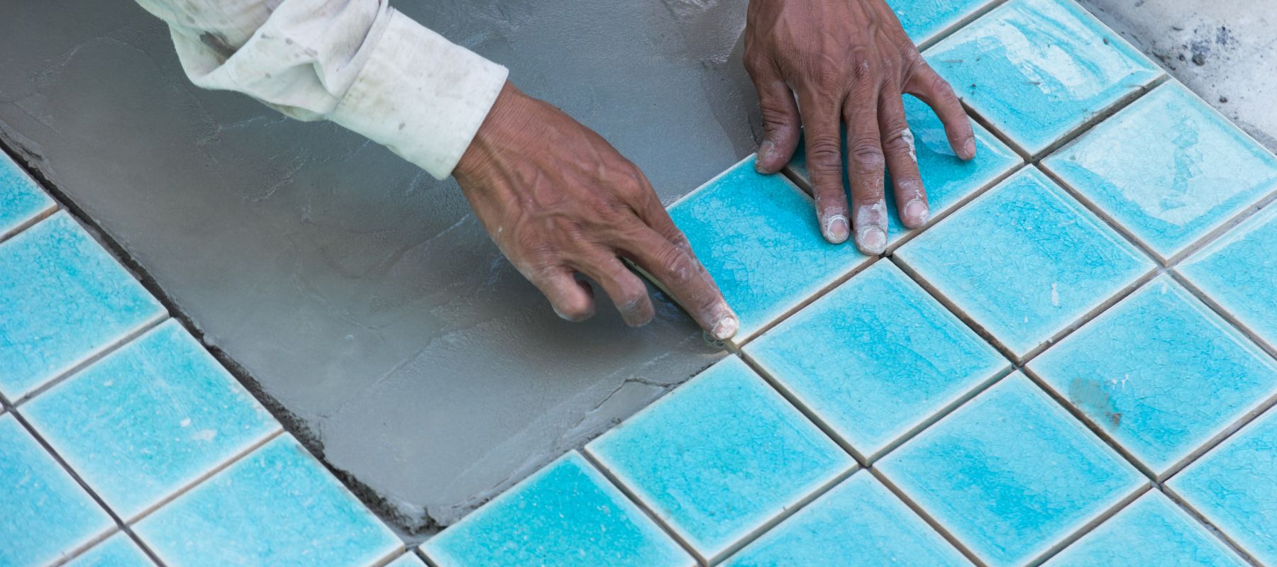 person carefully placing blue pool tiles